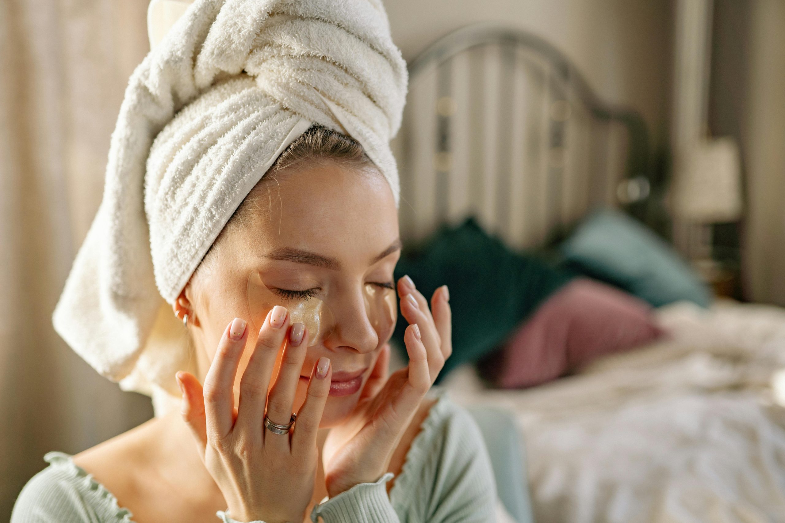 Woman enjoying a skincare routine with an under eye mask in a cozy bedroom setting.